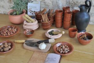 Photo d'un ensemble d'ustensiles de cuisine (petits bols en terre, carafe en étain, pilon en bois, etc.) et d'ingrédients prêts pour l'atelier "cuisinons romain" au musée d'ambrussum).