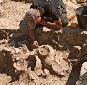 zoom sur un archéologue en train de dégager au pinceau une poterie