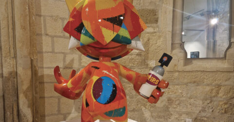 Statuette en résine représentant un personnage imaginaire et coloré avec une majorité d'orange et des tâches de rouge, bleu et jaune. Il tient dans sa main gauche une bombe de peinture pour les graffitis.