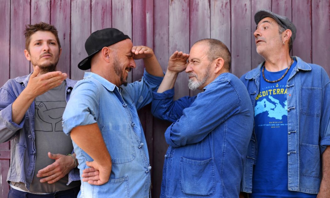 Photo des membres du groupe de musique Moussu T e lei Jovents. Deux des me,mbre au centre de l'image sont face à face et se regadent avec la main au dessus des yeux. Les deux autres, l'un à gauche et l'autre à droite regardent au loin.