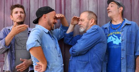 Photo des membres du groupe de musique Moussu T e lei Jovents. Deux des me,mbre au centre de l'image sont face à face et se regadent avec la main au dessus des yeux. Les deux autres, l'un à gauche et l'autre à droite regardent au loin.